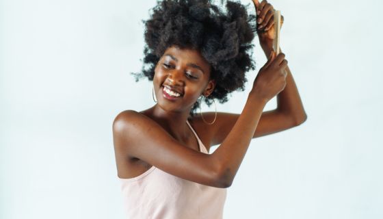 Smiling multiracial woman combing her black curly hair, neutral background.
