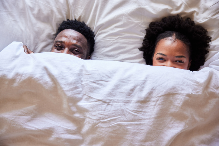 Smiling young couple peeking over their bed sheets in the morning