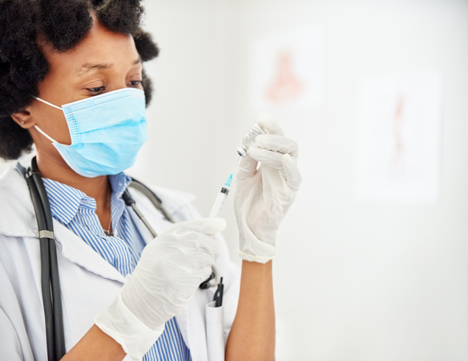 Doctor wearing face mask filling a syringe with vaccine in clinic
