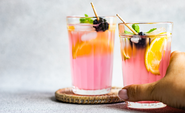 Woman reaching for a pink blackberry and lemon cocktail