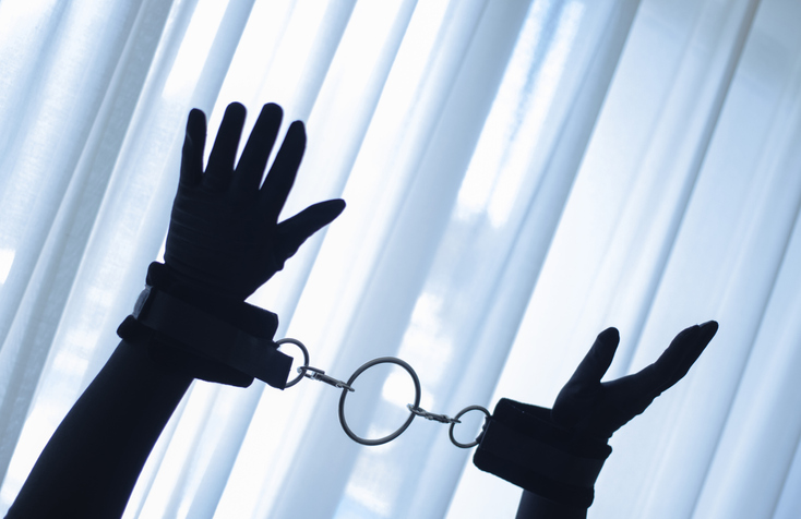 Cropped Hands Of Silhouette Person With Handcuffs Against Window