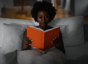 Black woman in bed reading erotic novels for women