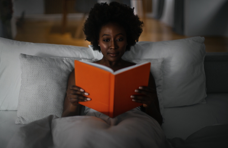 Black woman in bed reading erotic novels for women
