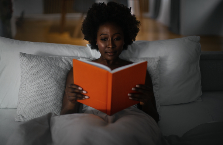 Black woman in bed reading erotic novels