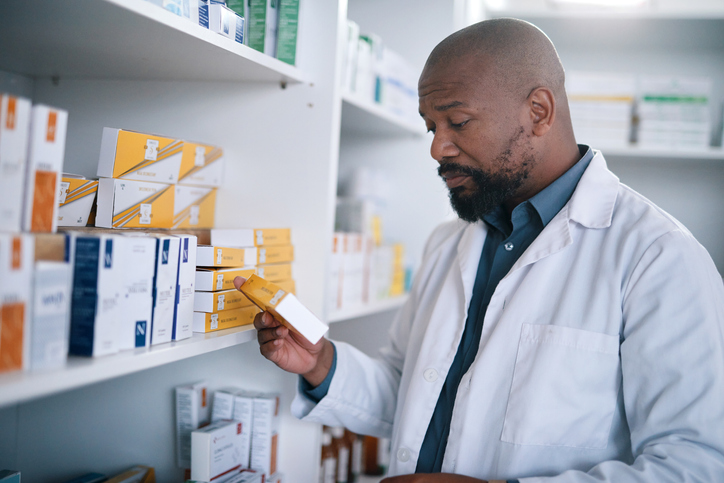 Medical pills, healthcare and African pharmacist or doctor working with medicine box on shelf of wellness pharmacy. Black man in pharmaceutical clinic reading information on stock for hospital