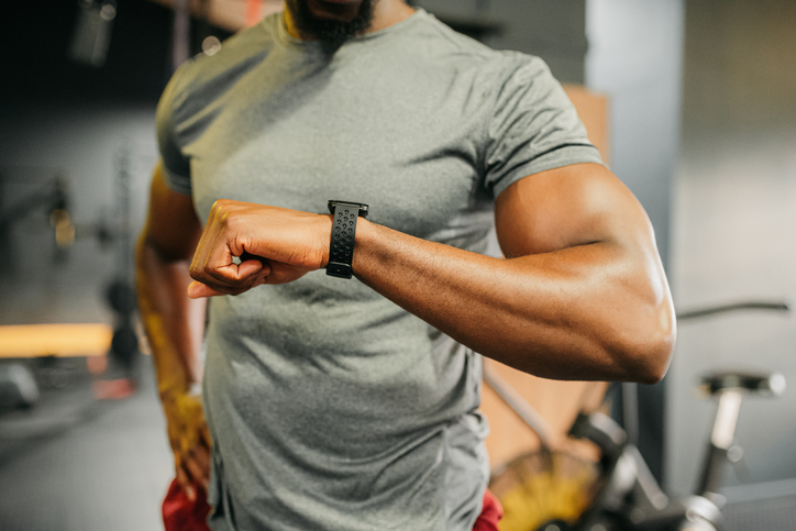 Sport, time and fitness with a sports man tracking his workout progress with an app on a watch in a gym. Exercise, training and health with a male athlete working out and exercising for wellness
