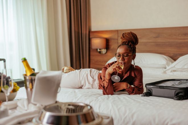 Wealthy woman lying on bed drinking wine in hotel.