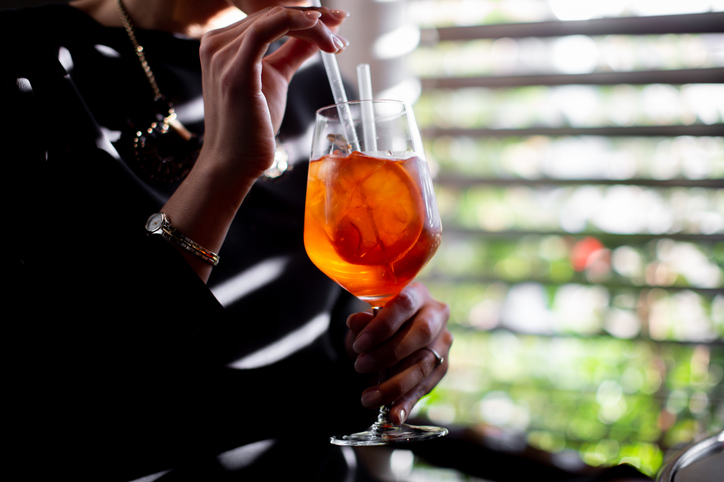 Cropped shot of young woman drinking spritz cocktail in boutique hotel restaurant, Italy