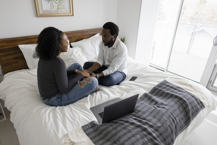 Couple talking face to face on bed during online marriage counseling