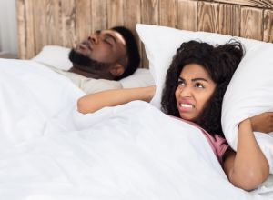 Angry black woman covering her ears with pillow considering a sleep divorce
