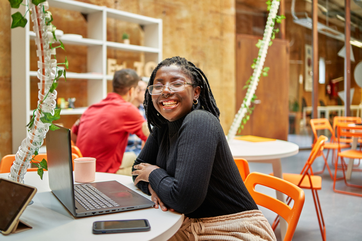 A young businesswoman sitting in her coworking space with her laptop and smiling while looking at camera