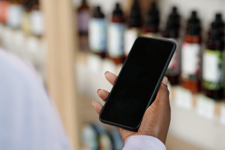 Hand of young black woman holding smartphone while standing in front of display