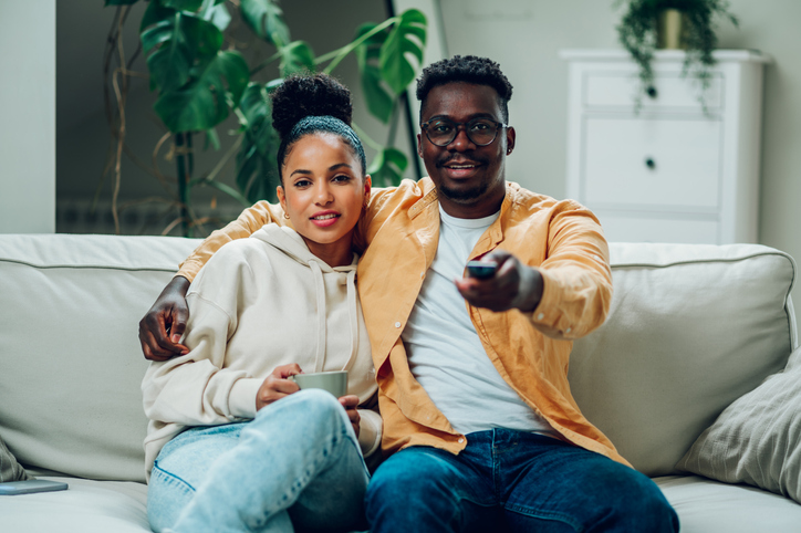 Multiracial couple watching television together at home on the couch involved in serial monogamy