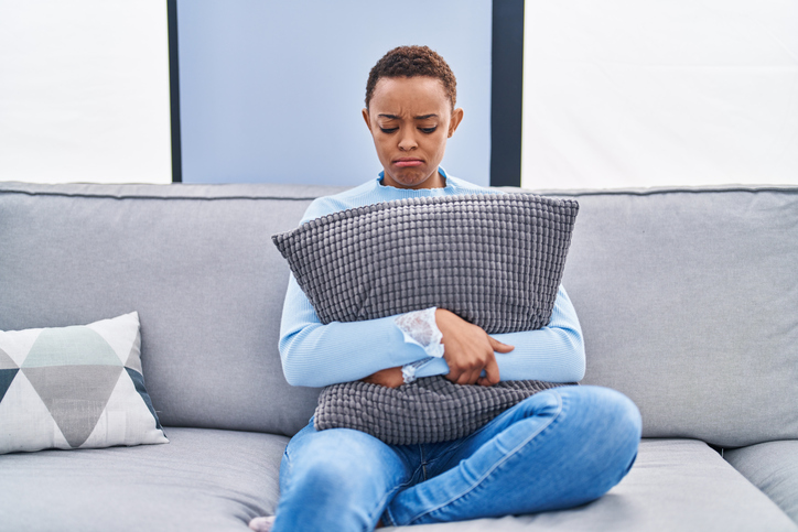 African american woman sitting on the sofa at home hugging pillow depressed and worry for distress, crying angry and afraid. sad expression.