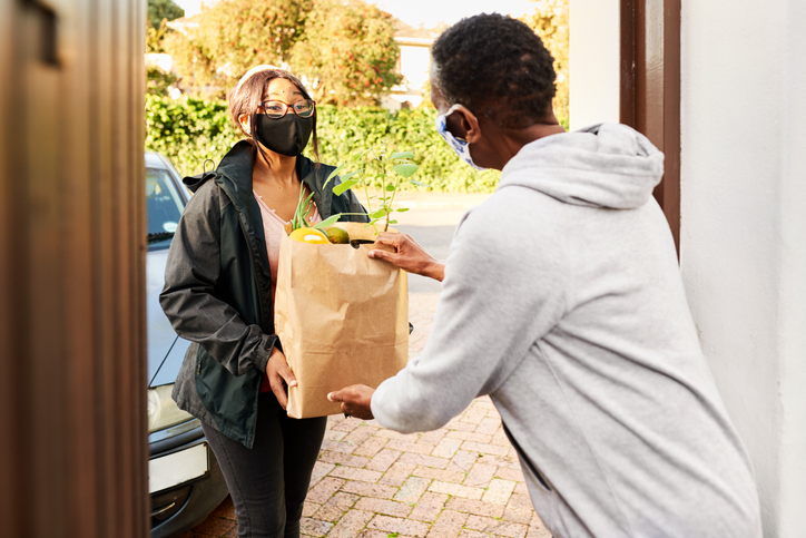 Woman in a face mask delivering groceries to a senior woman's home