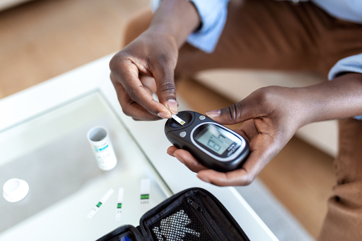 Young african man using digital glucometer at home. Diabetes control