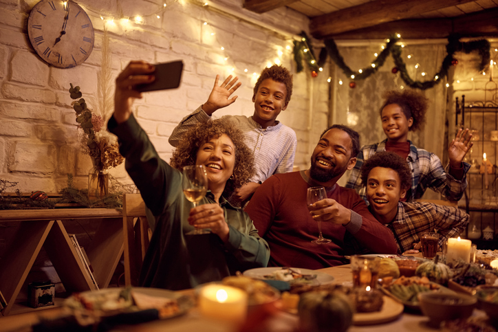 Cheerful black extended family taking selfie during Thanksgiving dinner in dining room.