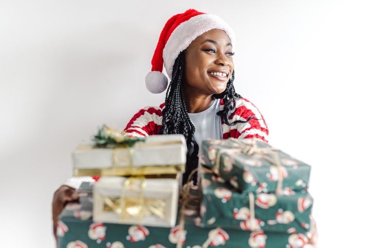 Cheerful African-American woman holding Christmas presents in front of the white background