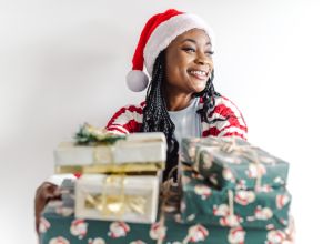 Cheerful African-American woman holding Christmas presents in front of the white background