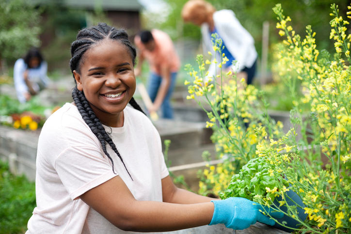 Portrait of Black young woman working smiling in community garden park with group of volunteers teamwork outdoors in neighborhood environment