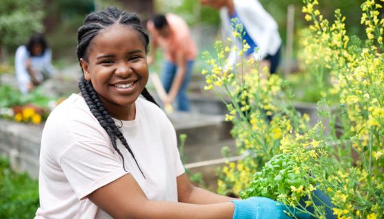 Portrait of Black young woman working smiling in community garden park with group of volunteers teamwork outdoors in neighborhood environment