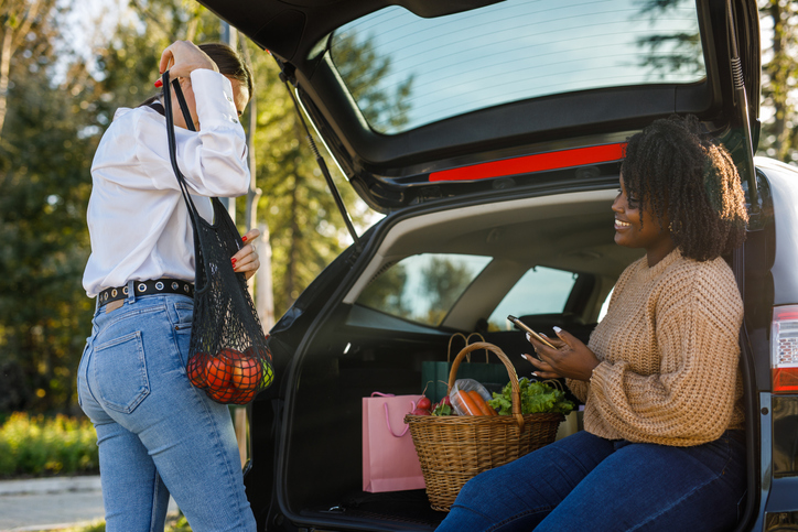 Two diverse girlfriends loading fresh produce in a car trunk after going shopping together