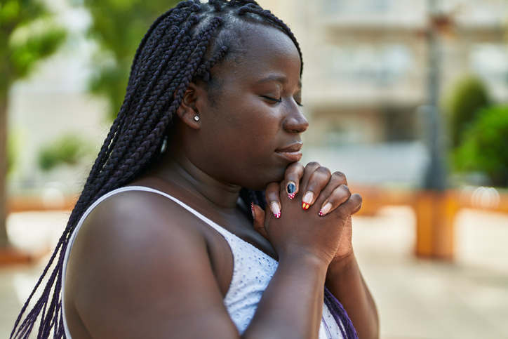 African american woman praying with closed eyes at park for human rights