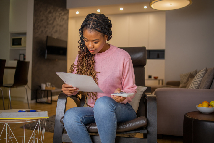 Young woman using calculator while going through bills and home finances