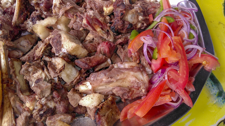 Close up of sharing platter of a traditional Kenyan dish, Nyama choma with accompaniment of kachumbari salad, of tomatoes and red onion.