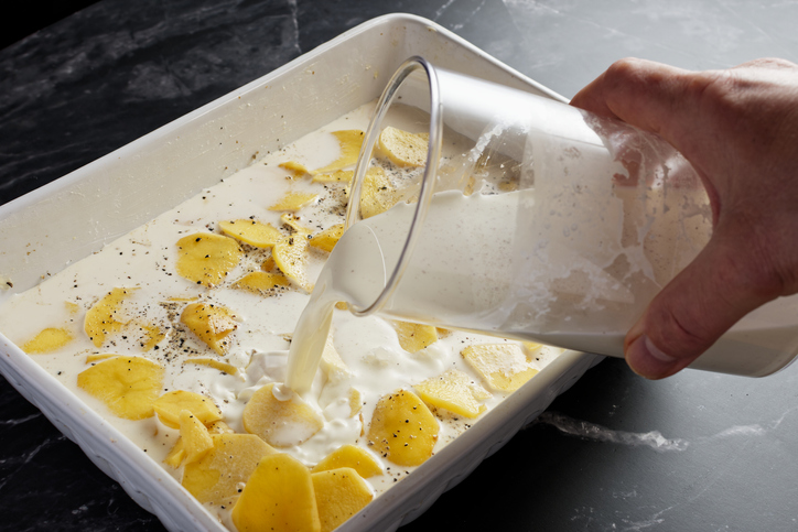 Poured potatoes for gratin Dauphinois in baking dish, pour over cream milk.