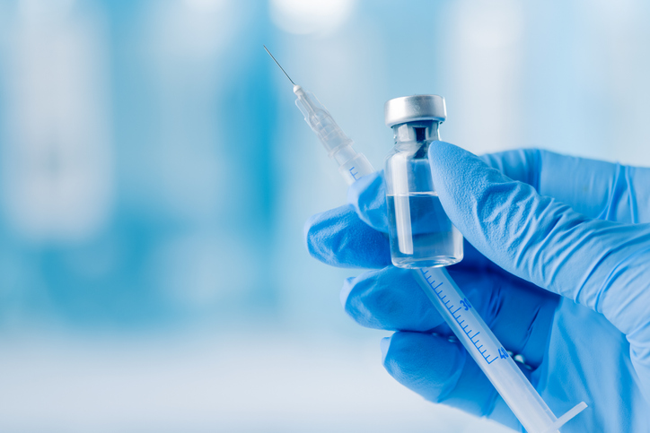 Doctor's hand holding glass vial and syringe with injection over blue background.