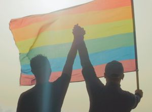 Two gay man celebrating LGBT pride month. Holding hands in air and waving rainbow flag celebrating Respect for Marriage Act