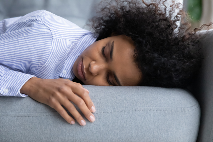 Exhausted young African American woman sleeping on sofa.