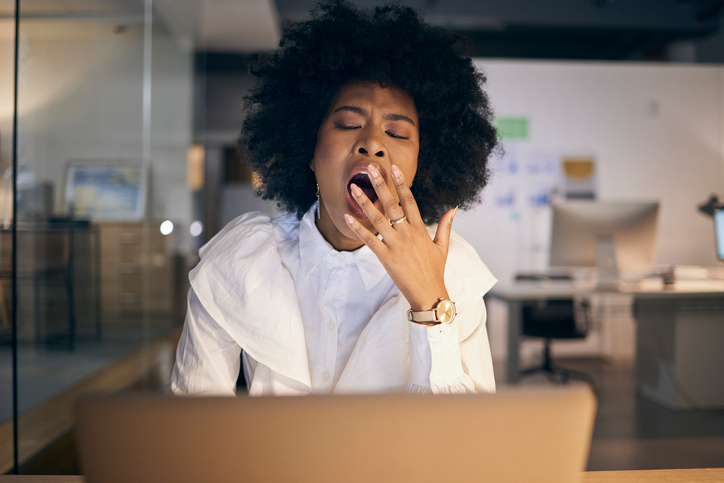 Tired, burnout and business woman yawning with a laptop at night in a dark office. Stress, fatigue and African corporate worker reading a proposal on the internet with a yawn during overtime