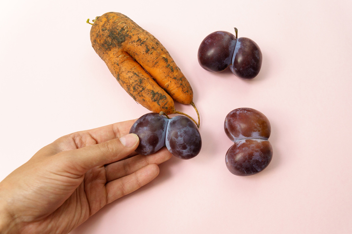 Ugly plums and carrot on pink background. fruits are suitable for food. Concept Reduction of organic food waste.