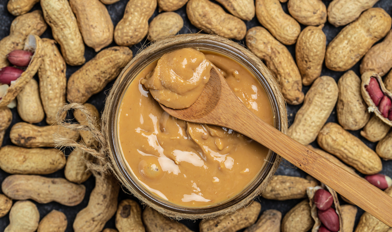 peanut paste in an open jar. creamy peanut butter peanuts scattered. top view