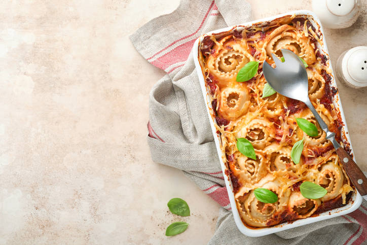 Lasagna. Homemade lasagna pasta rotolo bake with tomato sauce, cream cheese and basil on white skillet on light slate, stone or concrete background. Italian cuisine concept. Top view with copy space.