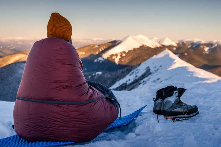 Young Woman Bivouacs At Snowy Mountain Range With The Snowy Range Mountains in the Background. First Morning Light. enjoying one of her gifts for outdoor lovers