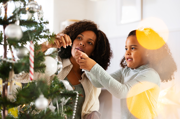 Mother with a cute little daughter decorating a Christmas tree at home for a winter holidays