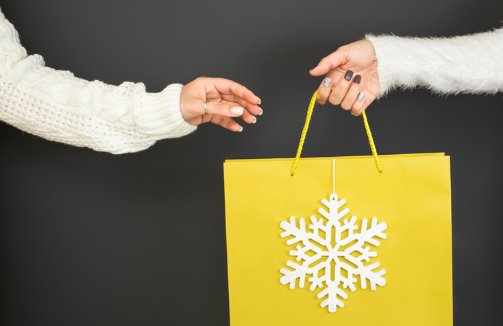 One female hand is passing a craft yellow paper bag to the other hand on grey background. Concept of thrift stores, resale, second hand.