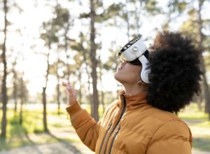 African american curly hair female with yellow coat and virtual reality goggles playing in the forest