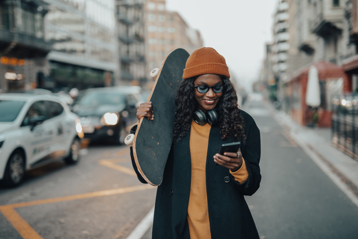 A young black woman, hipster style, with a skateboard in her hands walks down the street of Barcelona