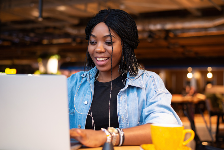 An African-American black woman smiles while looking at a laptop. Coworking