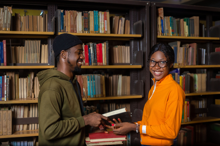 Cheerful African American students exchanging books at a library