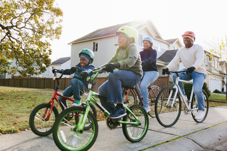 Family Riding Bicycles On Neighborhood Street