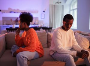 Upset african couple have problems in marriage, sitting back to back on sofa at home and not talk