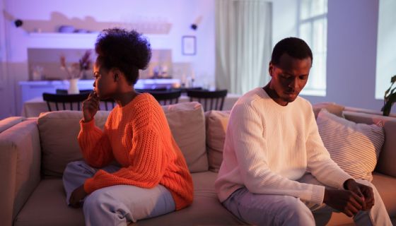 Upset african couple have problems in marriage, sitting back to back on sofa at home and not talk