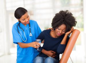 caring african american nurse offering sick patient water who has inflammatory bowel disease