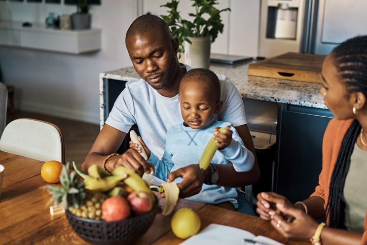 Banana, healthy and black family with baby eating fruits for morning breakfast protein and planning nutrition together. African father help child with fruit for growth development and talk to mother
