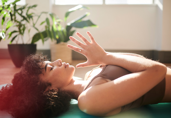 African American woman lying down in prayer pose. Daily yoga improves mindfulness and mental clarity. Spirituality and exercise combined bring about wellness for body and soul.